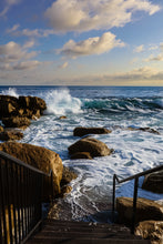 Stairs leading down to a rocky shoreline with waves crashing against the rocks.